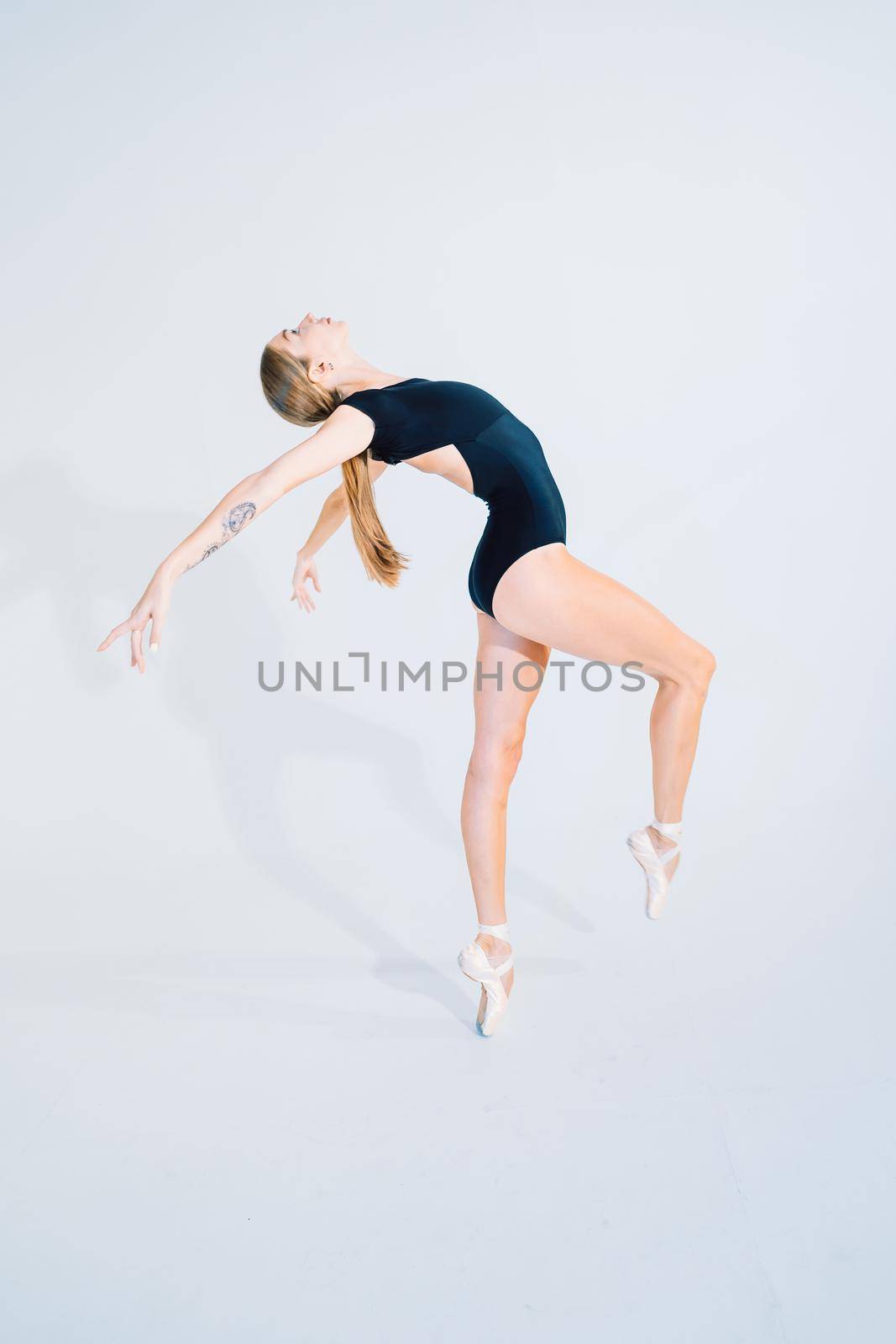 Ballerina in black bodysuit practicing on white studio background. Woman dancing classical pas. Alone warming up before performance. Amazing dance. High quality photo