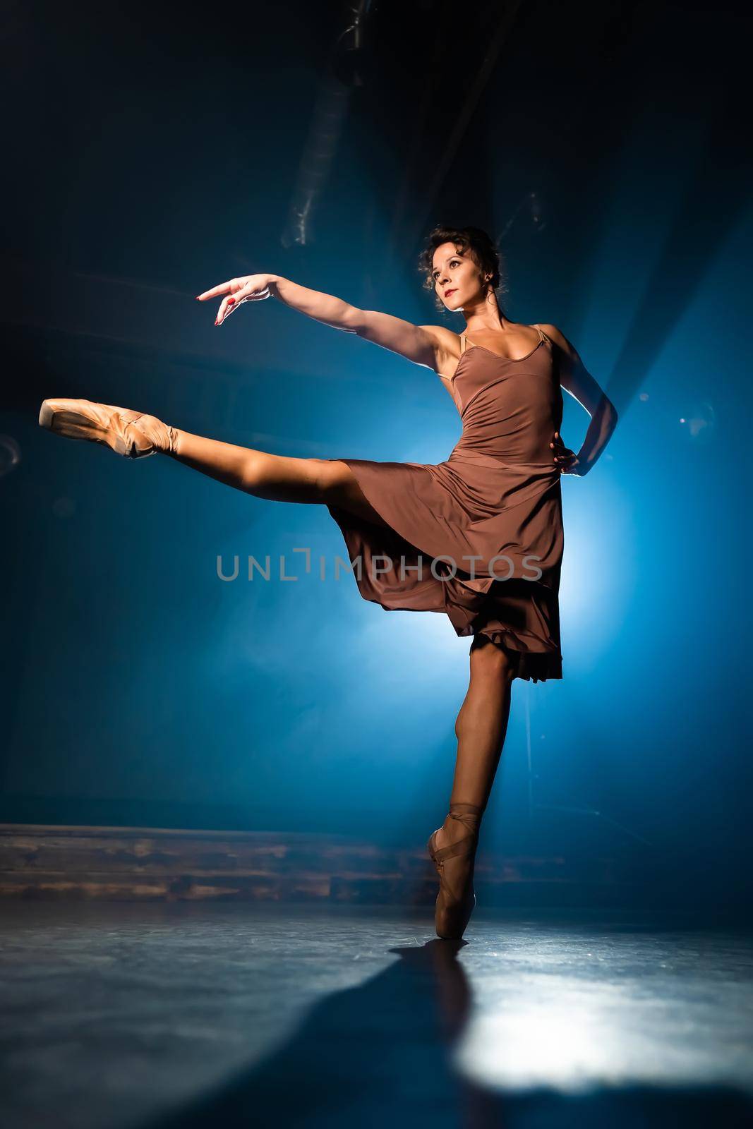 Graceful ballerina in dress dancing elements of classical or modern ballet in dark with floodlight backlight. Smoke on black background. Art concept. High quality photo