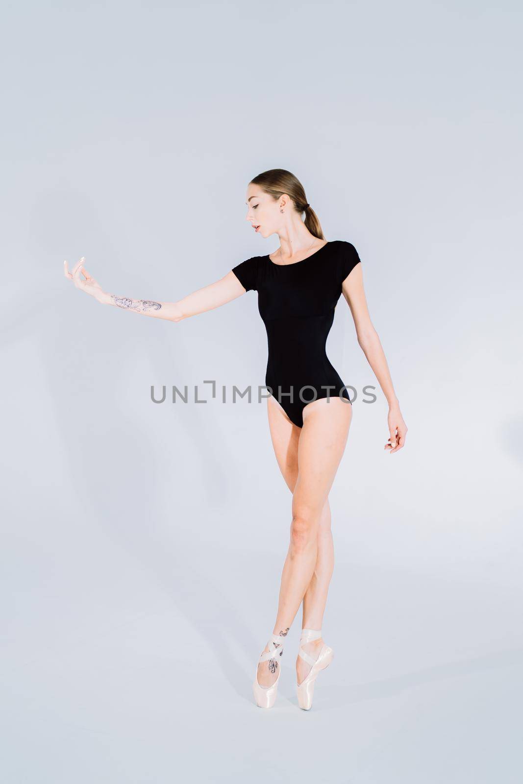 Ballerina in black bodysuit practicing on white studio background. Woman dancing classical pas. Alone warming up before performance. Amazing dance. High quality photo