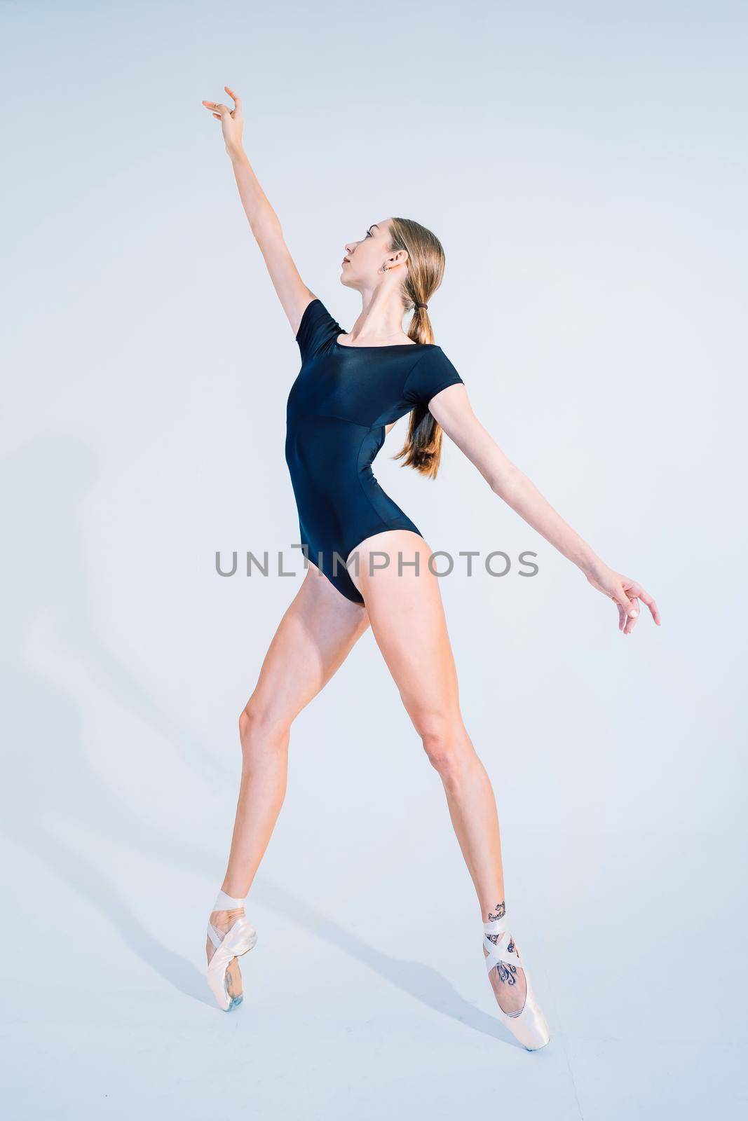 Ballerina in black bodysuit practicing on white studio background. Woman dancing classical pas. Alone warming up before performance. Amazing dance. High quality photo