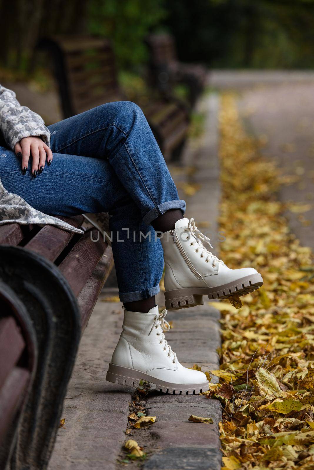 Female legs in a jeans and white fashion boots with laces. fallen leaves on the sidewalk