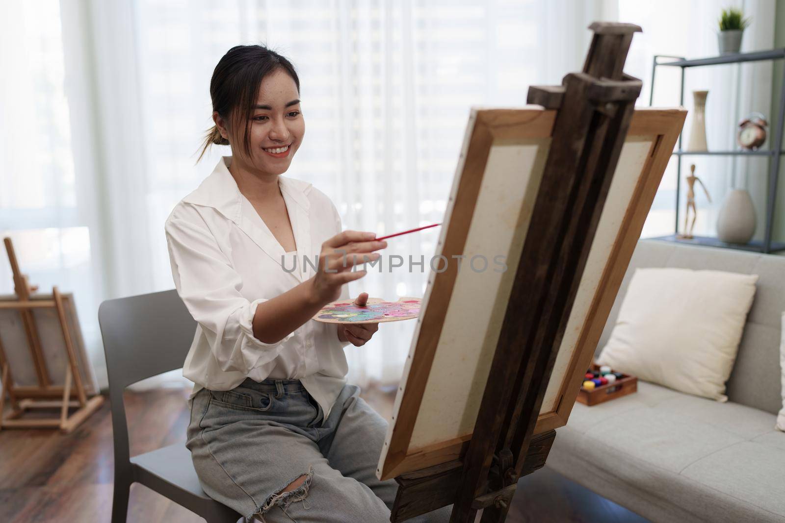 Joyful young female artist painting on canvas at workshop.