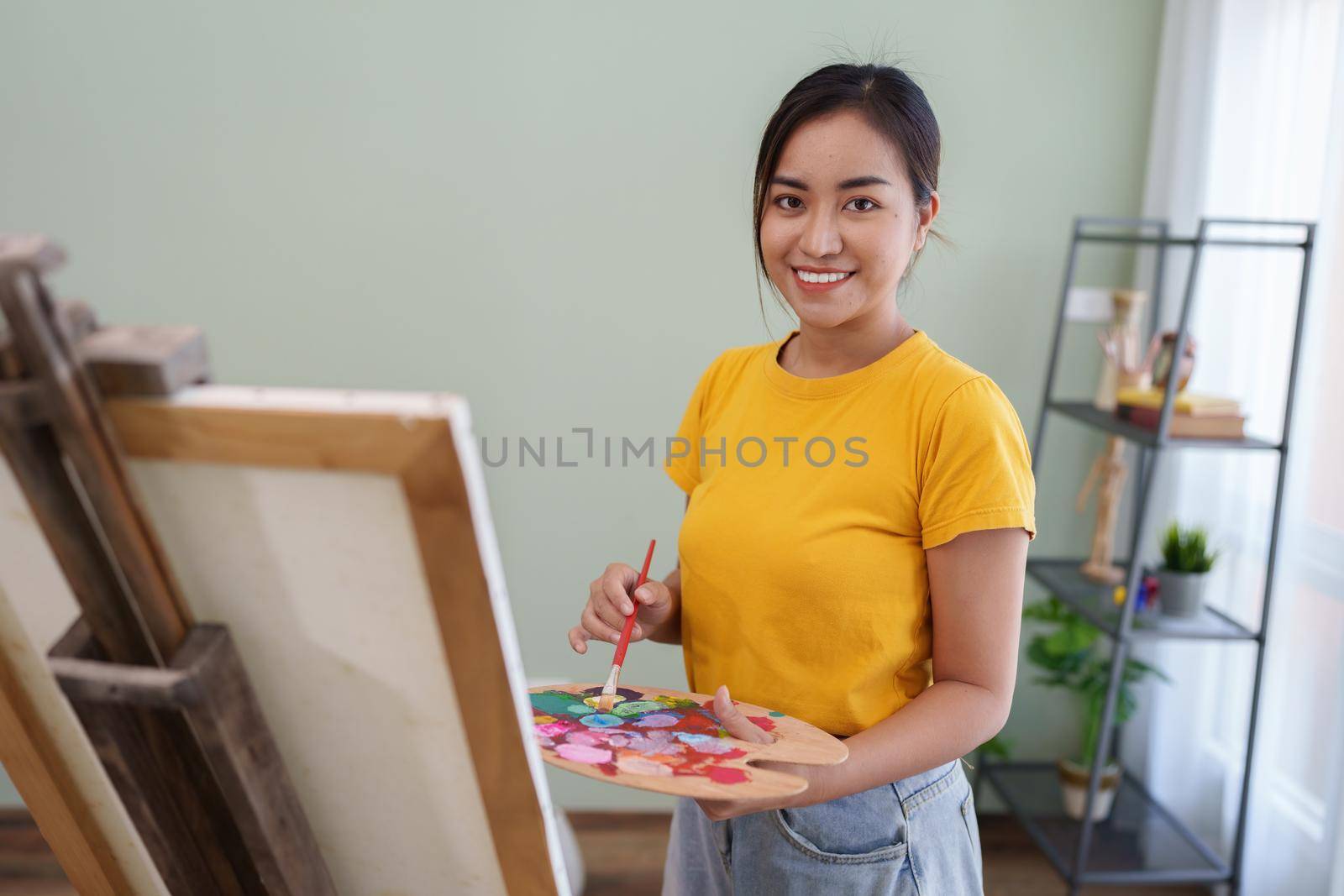 Joyful young female artist painting on canvas at workshop.