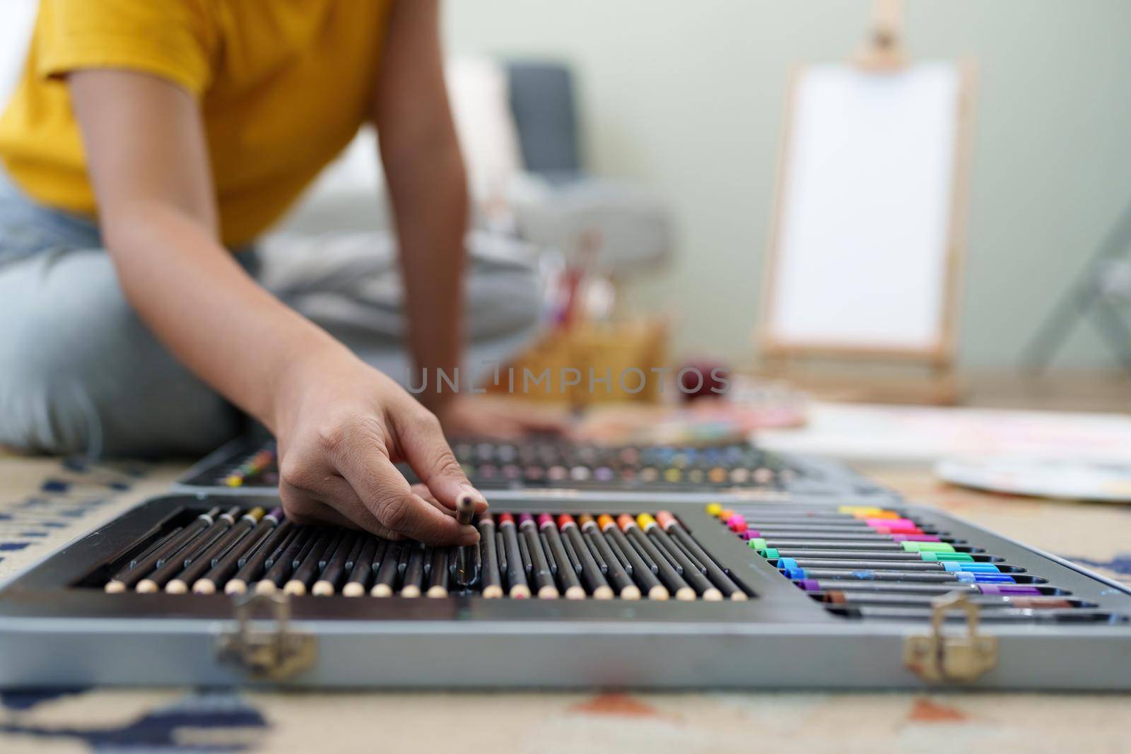 Joyful young female artist choosing colour pencil at workshop.