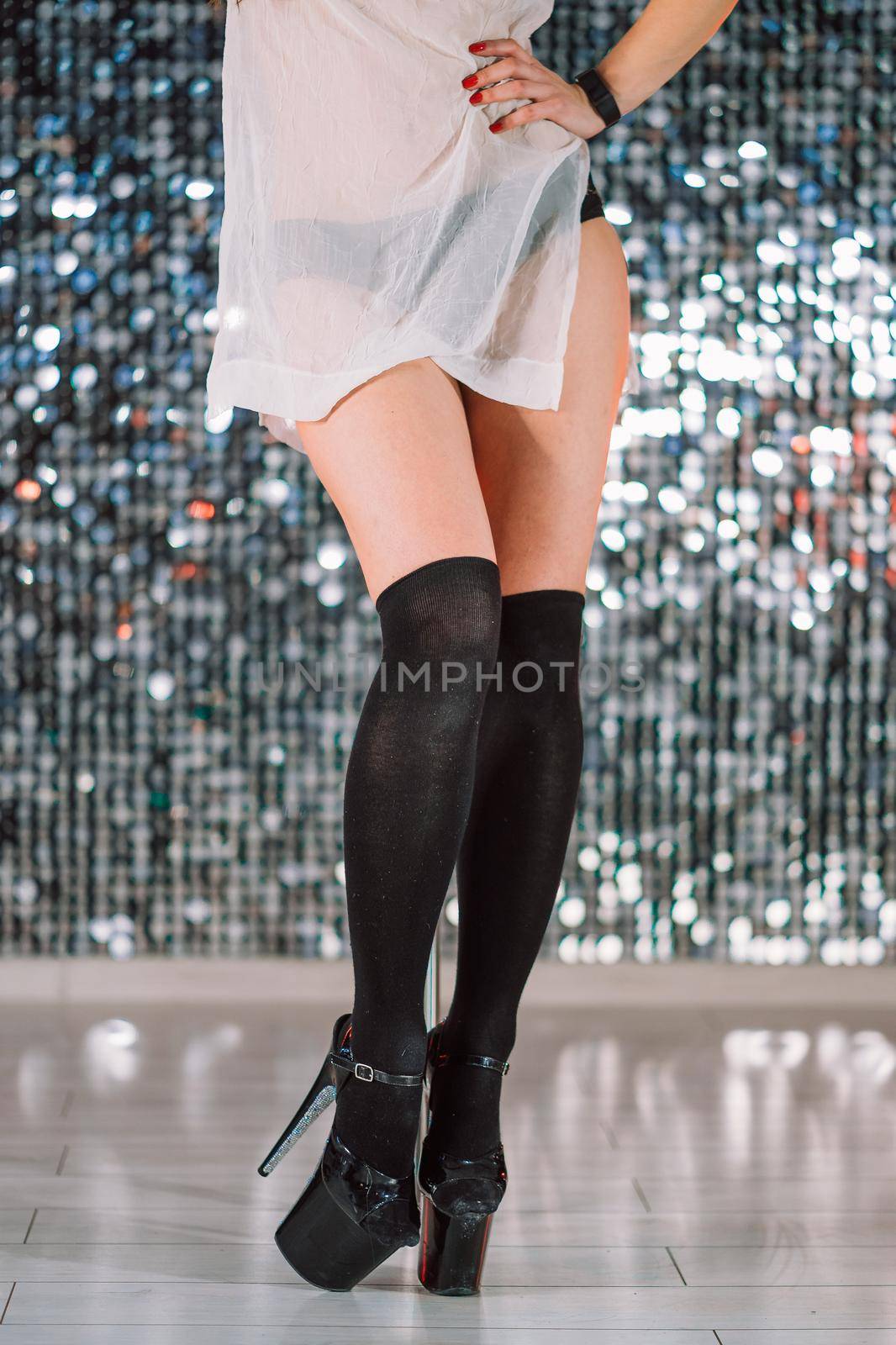Close-up legs of unrecognizable woman. Young stripper in black stockings in night men's club. Poledance on shining wall background. High quality photo