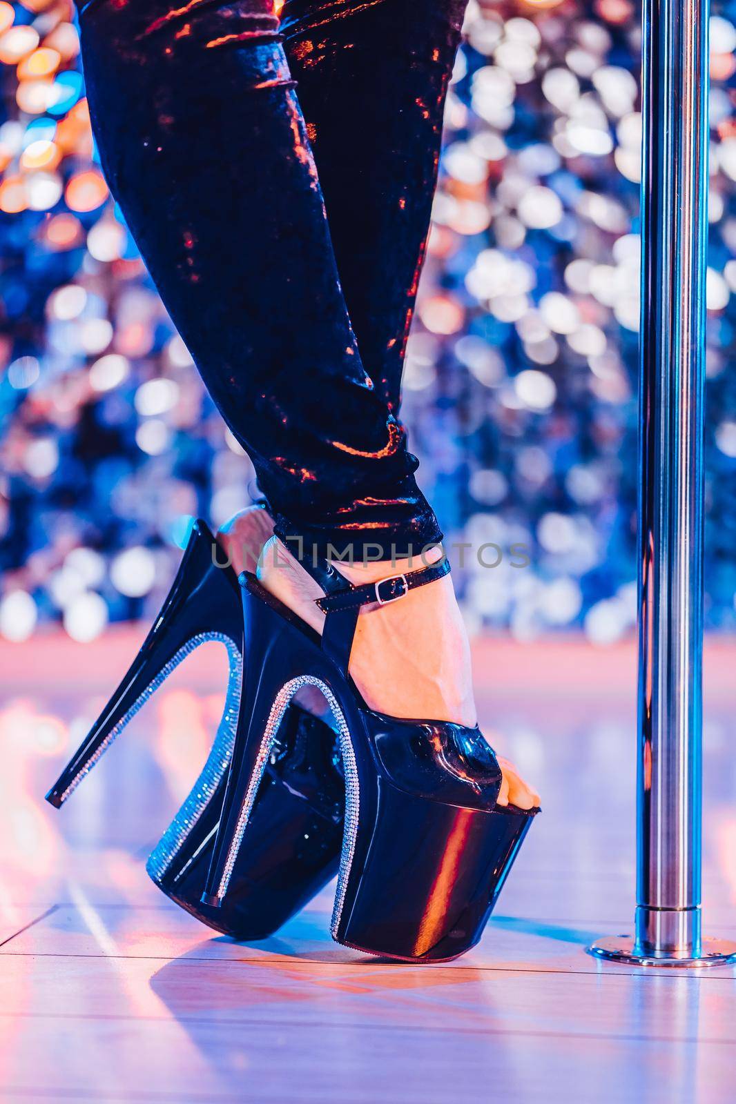 Legs in high sexy shoes near pylone. Striptease dancer moving on stage in strip night club. Pole dancing background. High quality photo