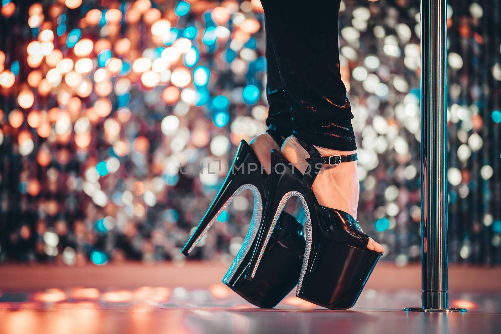 Legs in high sexy shoes near pylone. Striptease dancer moving on stage in strip night club. Pole dancing background. High quality photo