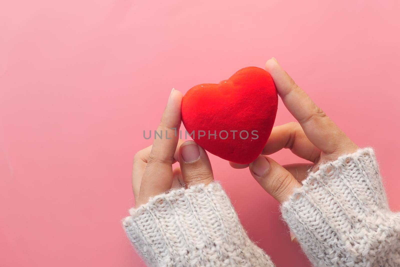 women hand holding red heart on pink background .