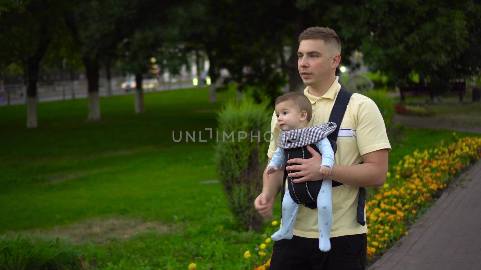 A young father walks with a child in the park. Newborn son in a kangaroo-backpack. Close-up. 4k