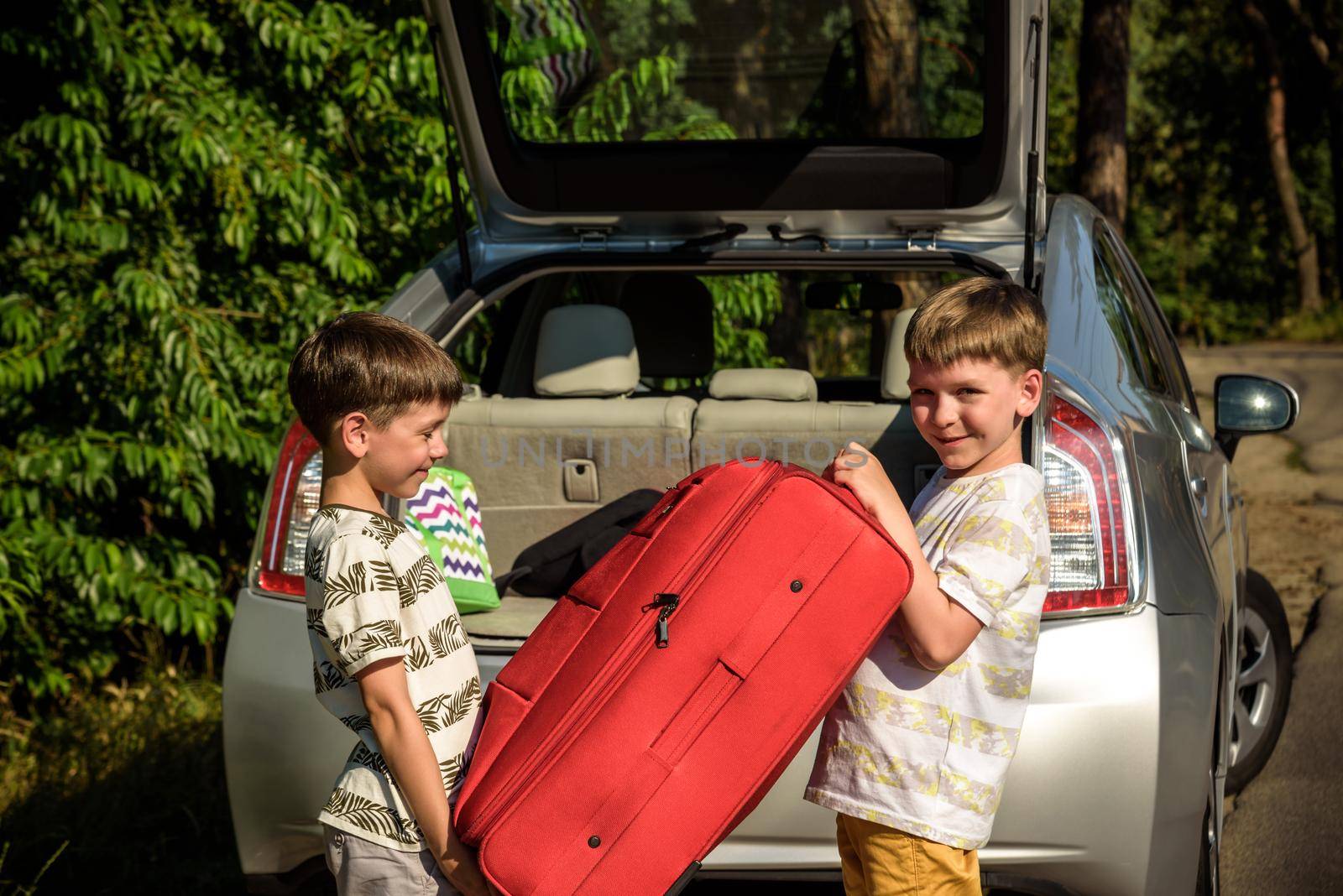 Two adorable boys holding a suitcase going on vacations with their parents. Two kids looking forward for a road trip or travel. Family travel by car.