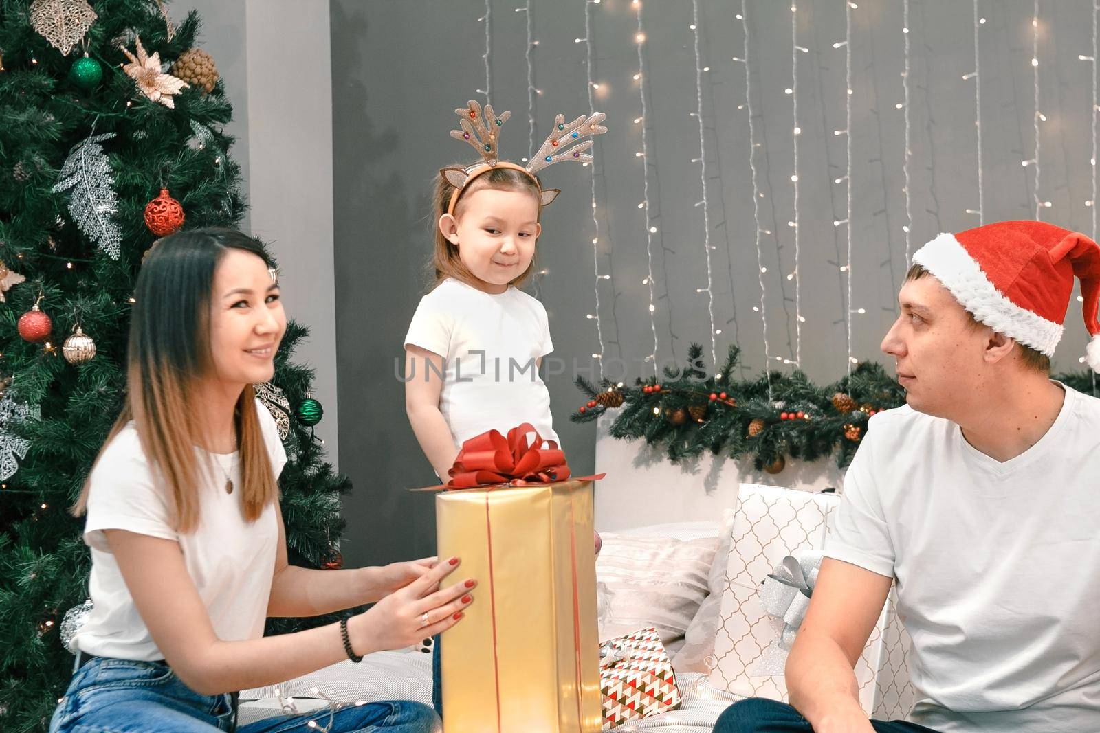 Cozy family christmas, father mother and child girl daughter play and have fun with gifts in bedroom, happy cheerful xmas holiday together, authentic festive lifestyle, gray interior