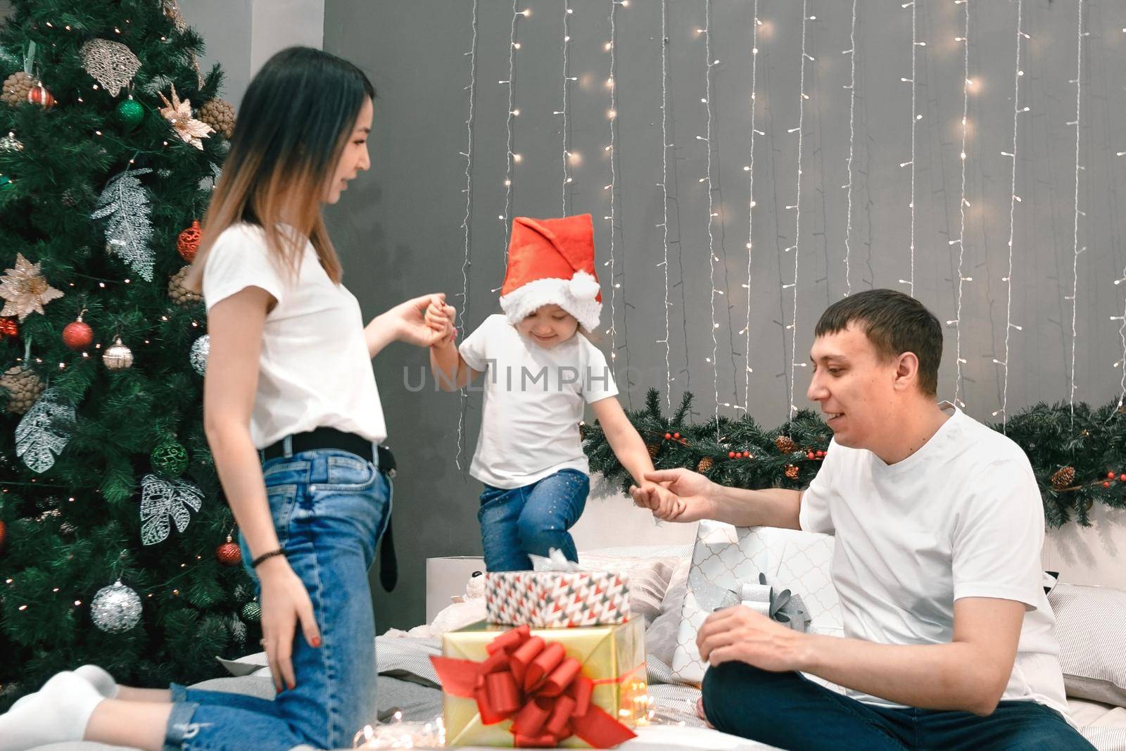 Cozy family christmas, father mother and child girl daughter play and have fun with gifts in bedroom, happy cheerful xmas holiday together, authentic festive lifestyle, gray interior