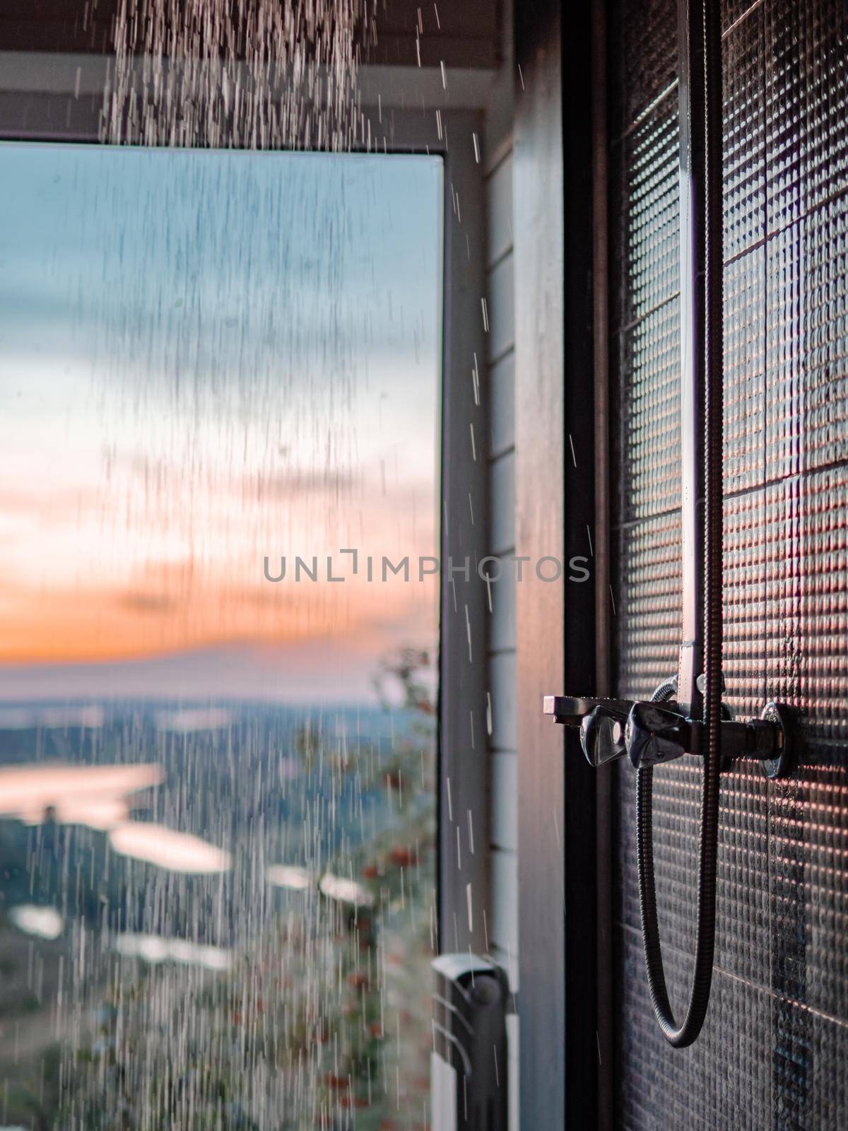 Bathing room interior with panoramic window. Splashes and drops of water from shower in bathroom with panoramic window in summer nature background at sunset.