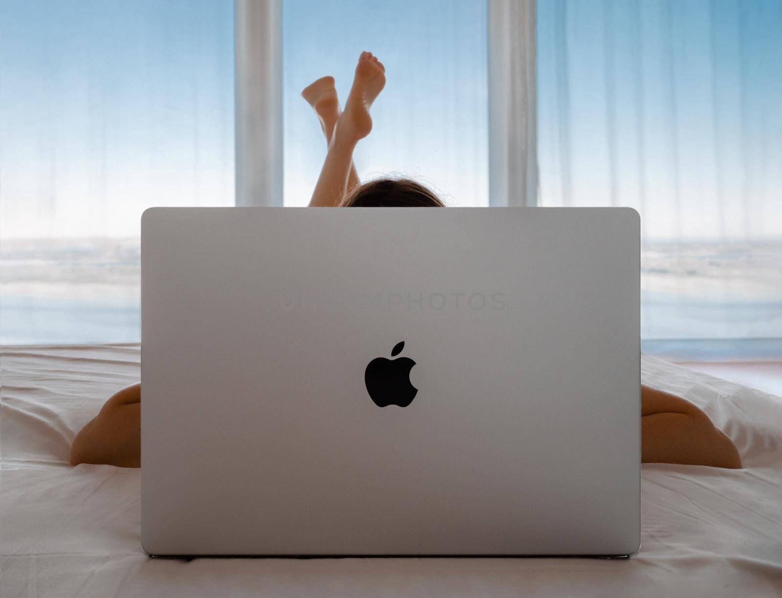 Womanl lying in bed using behind mackbook pro, panoramic windows, sea background by fascinadora