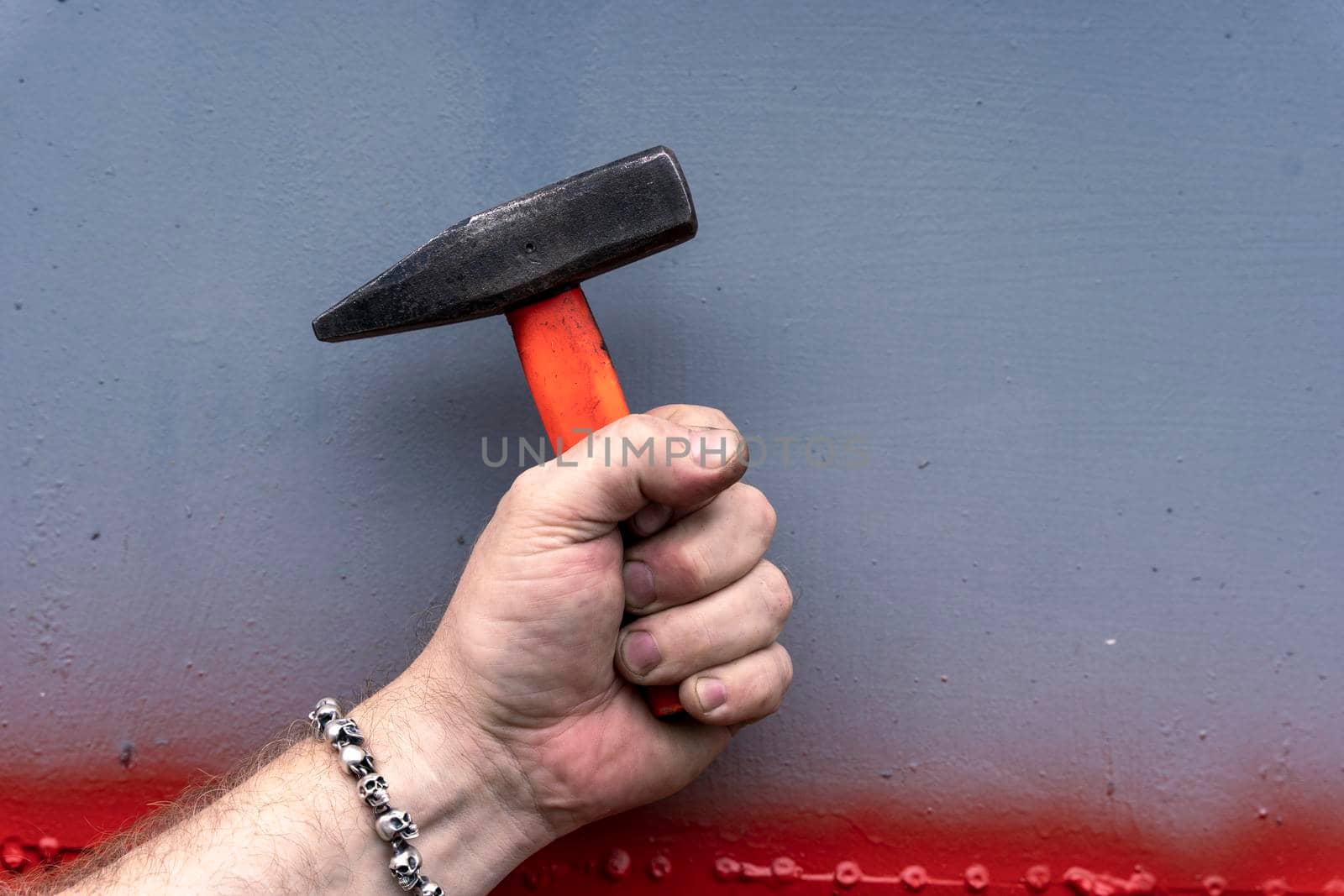 male hand holding a hammer with a short plastic handle on gray background