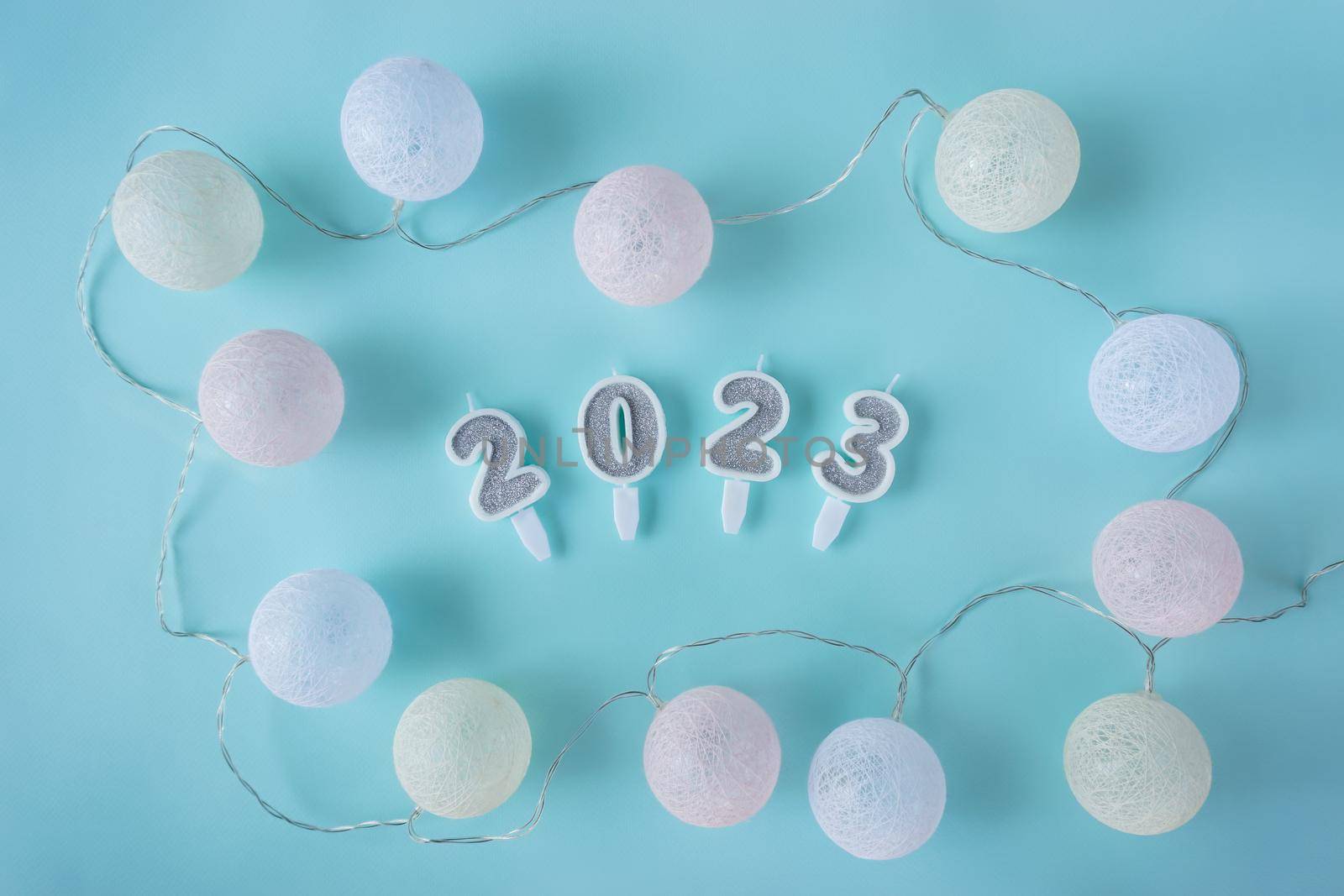 On a delicate pastel background are candles 2023 and round balls garlands. High quality photo