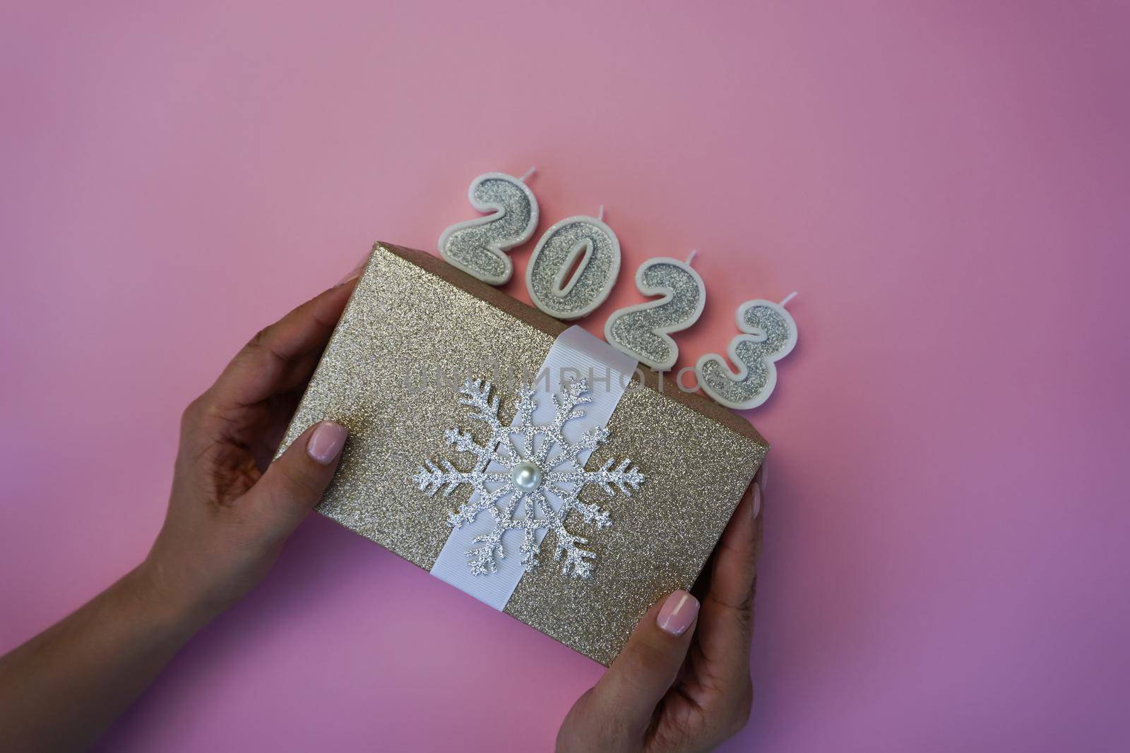 In women's hands is a box with a Christmas gift and candles in the form of numbers 2023. High quality photo