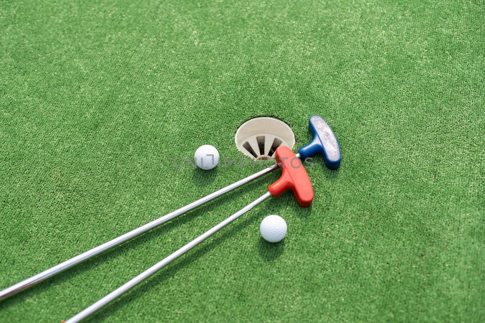 Mini-golf clubs and balls of different colors laid on artificial grass by Andelov13