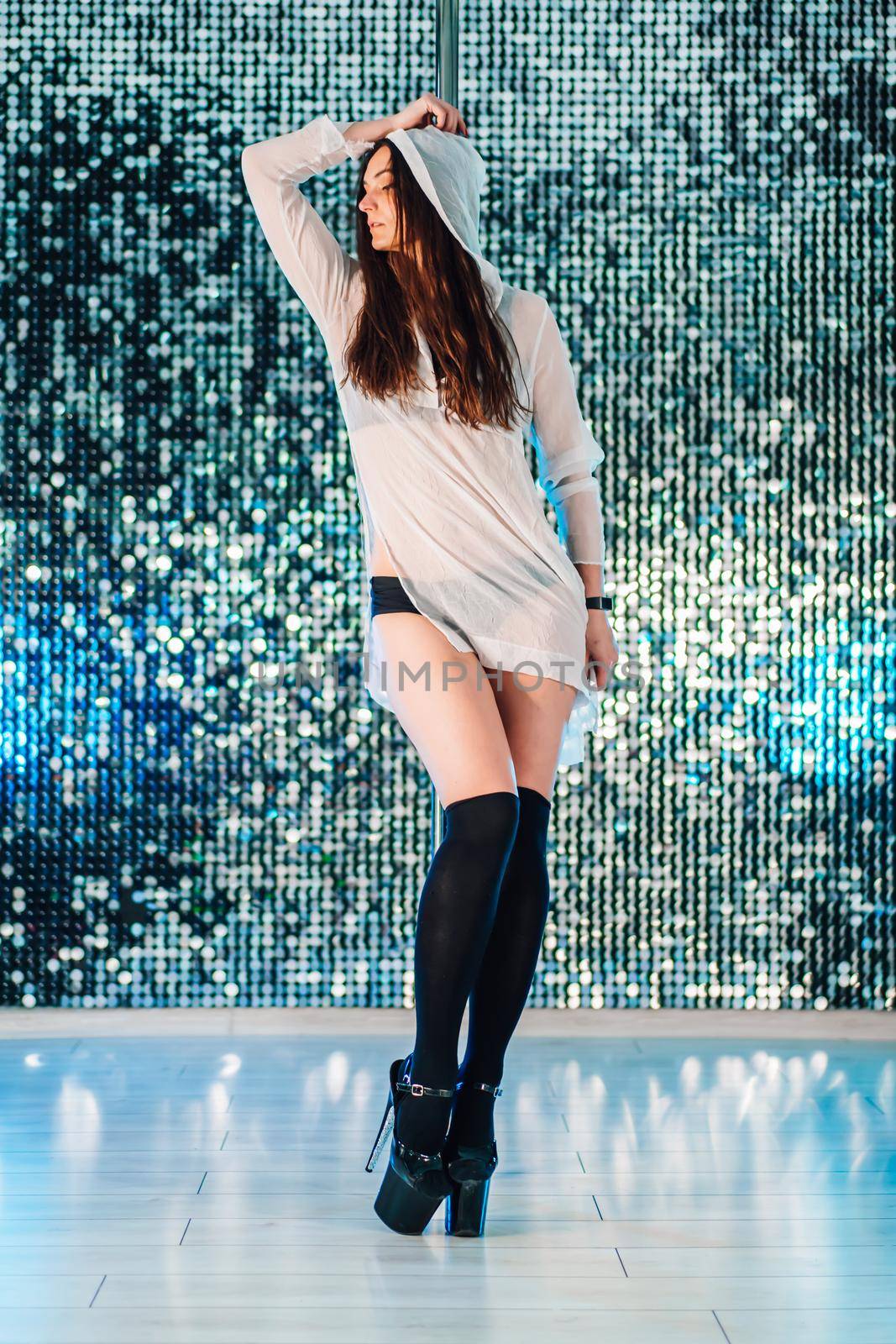 Alluring woman with long hair posing with pylon on shining wall background. Pole-dance, sexy, temptation concept. High quality photo