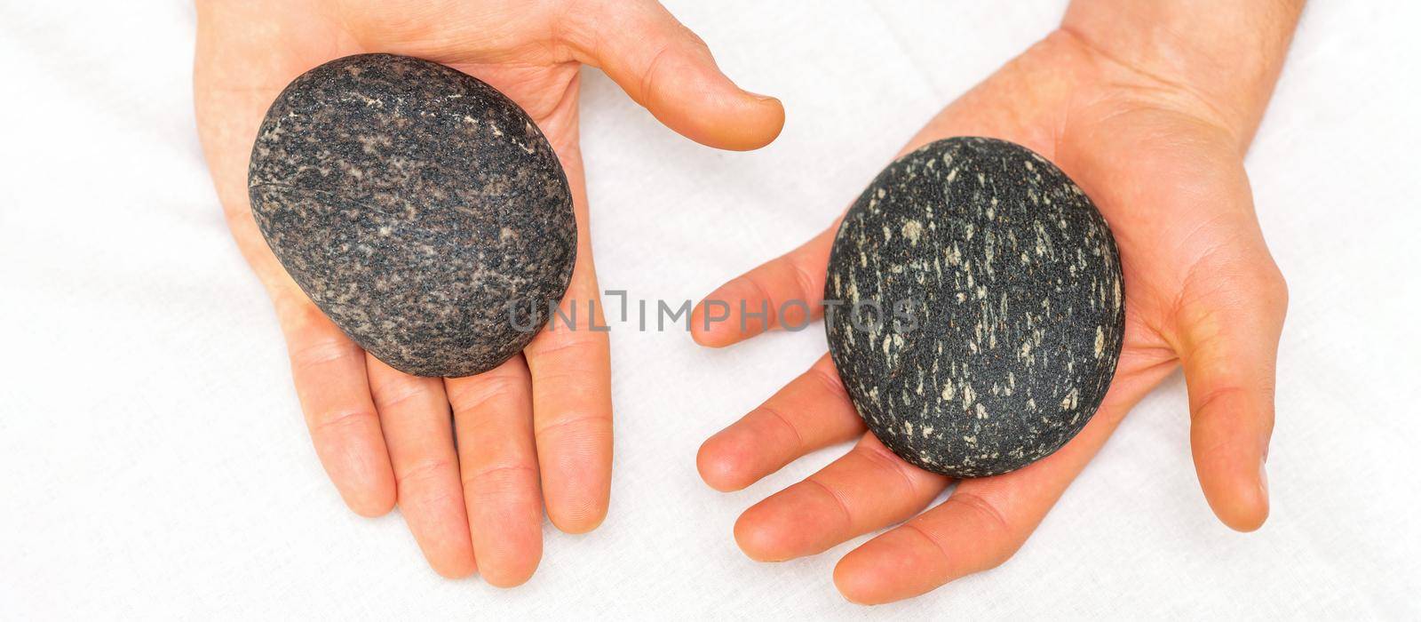 Top view of two male hands with black hot stones lying on a white towel in beauty spa