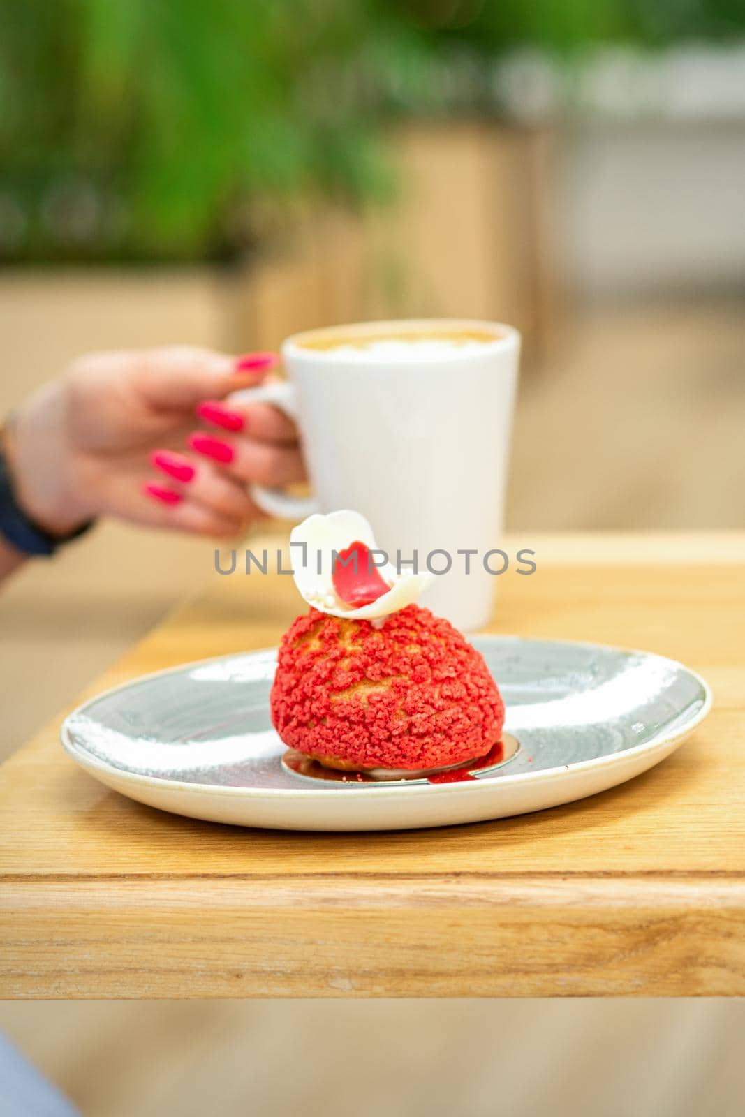 Young female drinking coffee with a piece of cake sitting at the table in a cafe outdoors