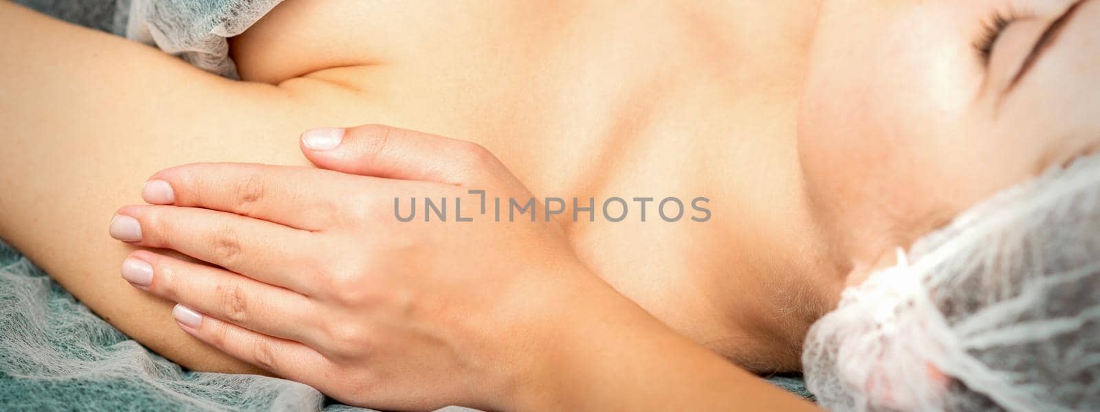 Side view hands of female therapist making massage of shoulders to young caucasian woman in spa beauty salon
