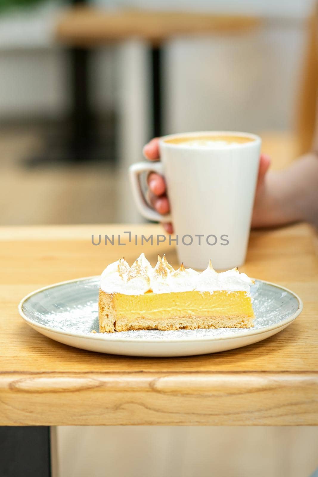 Young female drinking coffee with a piece of cake sitting at the table in a cafe outdoors