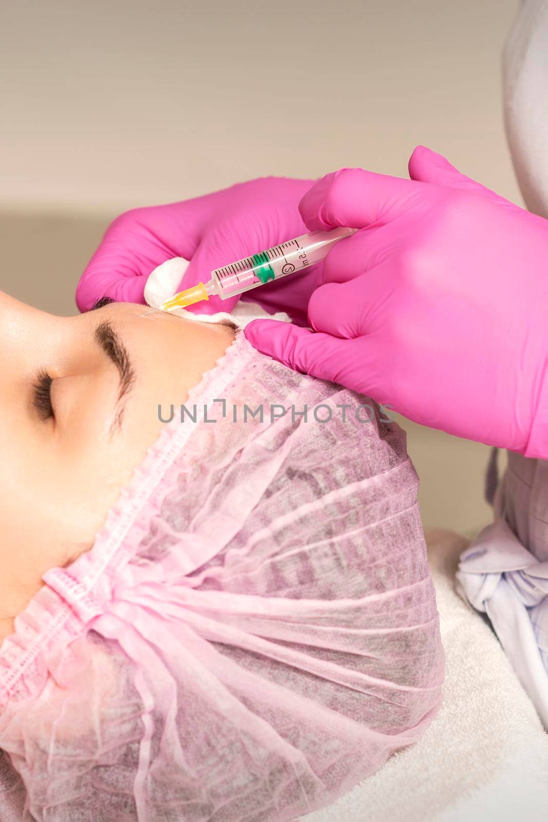 Young woman receiving an injection of anti-aging botox filler to the forehead from a cosmetologist in a beauty salon. Facial treatment injection
