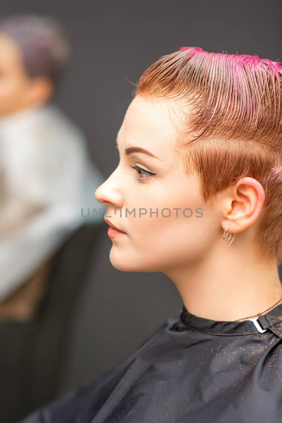 Side view portrait of a beautiful young caucasian woman with a short pink haircut waiting for a hairdresser in a beauty salon