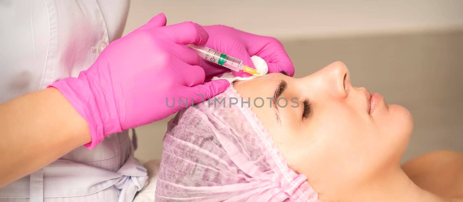 Young woman receiving an injection of anti-aging botox filler to the forehead from a cosmetologist in a beauty salon. Facial treatment injection