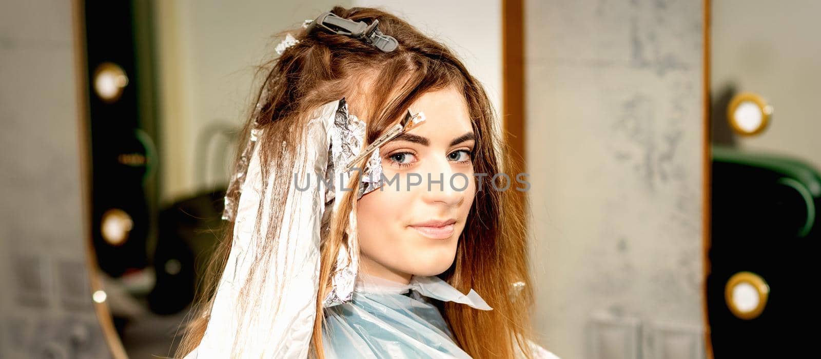 Portrait of a beautiful young caucasian woman getting foil on her hair before dyeing in a beauty salon