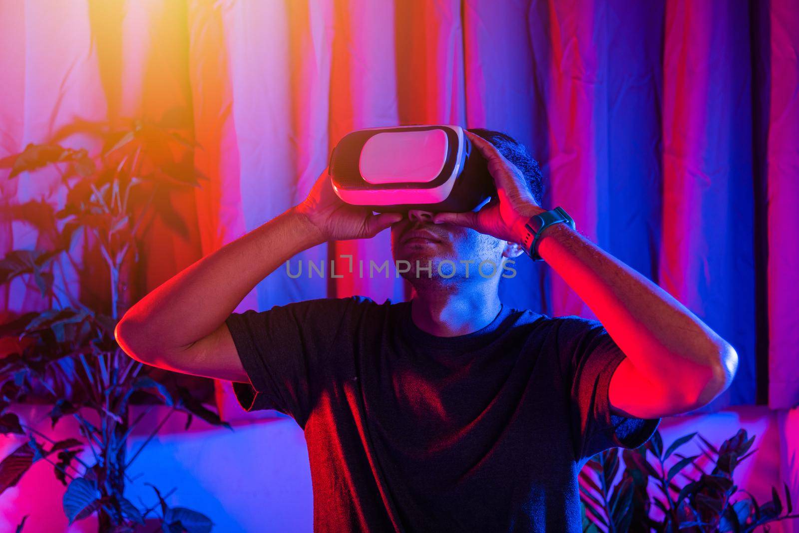 Asian handsome man wear VR helmet excited emotional at home purple and blue background, experiencing virtual reality goggles experiencing reality excited emotional, metaverse and cyberspace