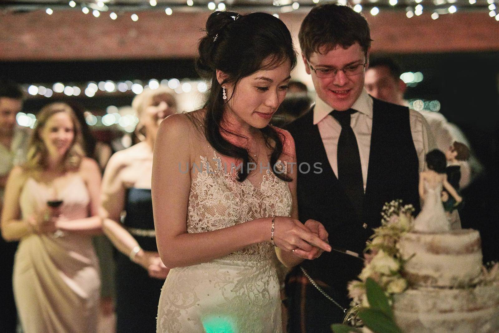 The cutting of the cake. a cheerful young bride and groom cutting the wedding cake together inside of a building during the day