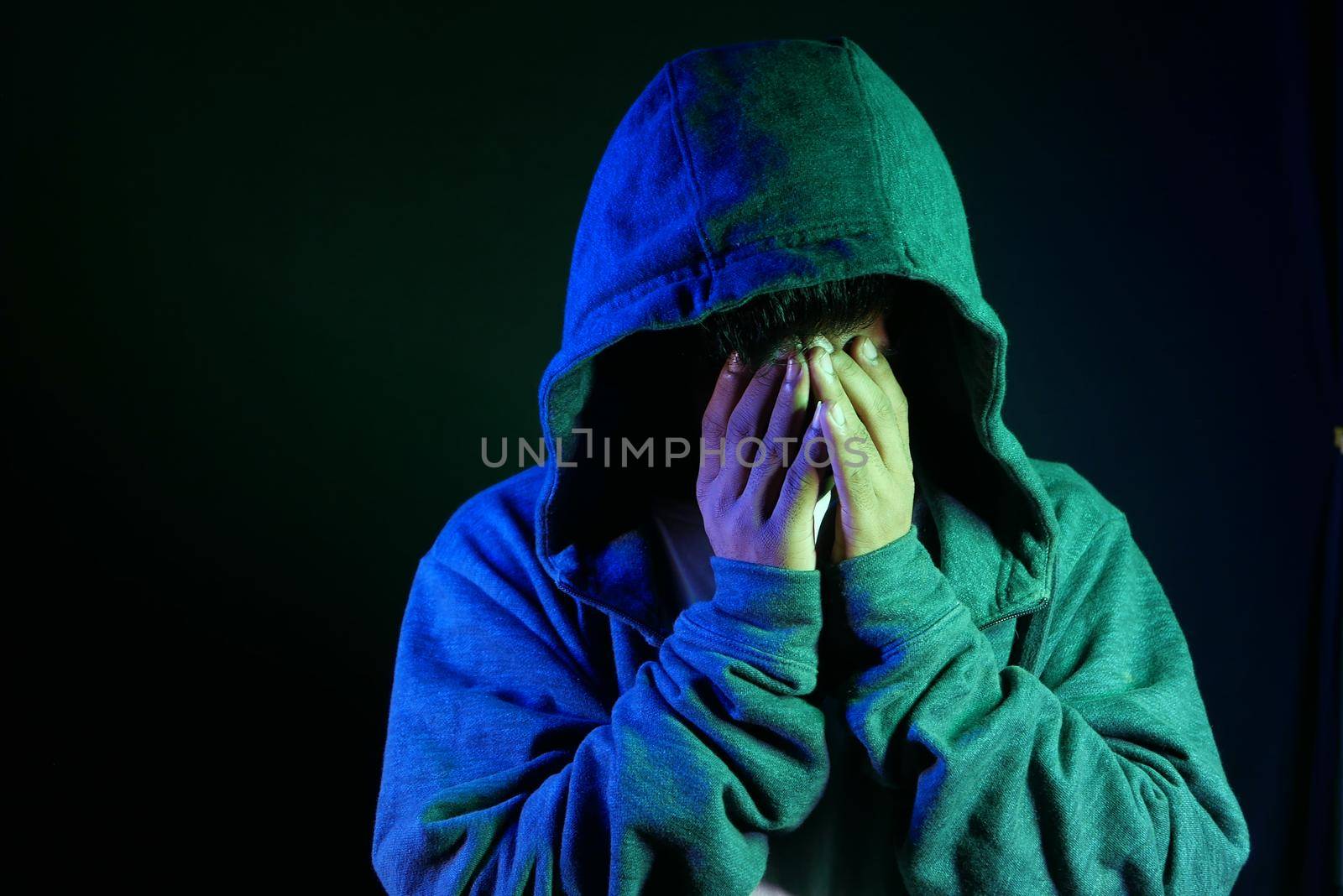 sad man in hood cover face with hands isolated in black