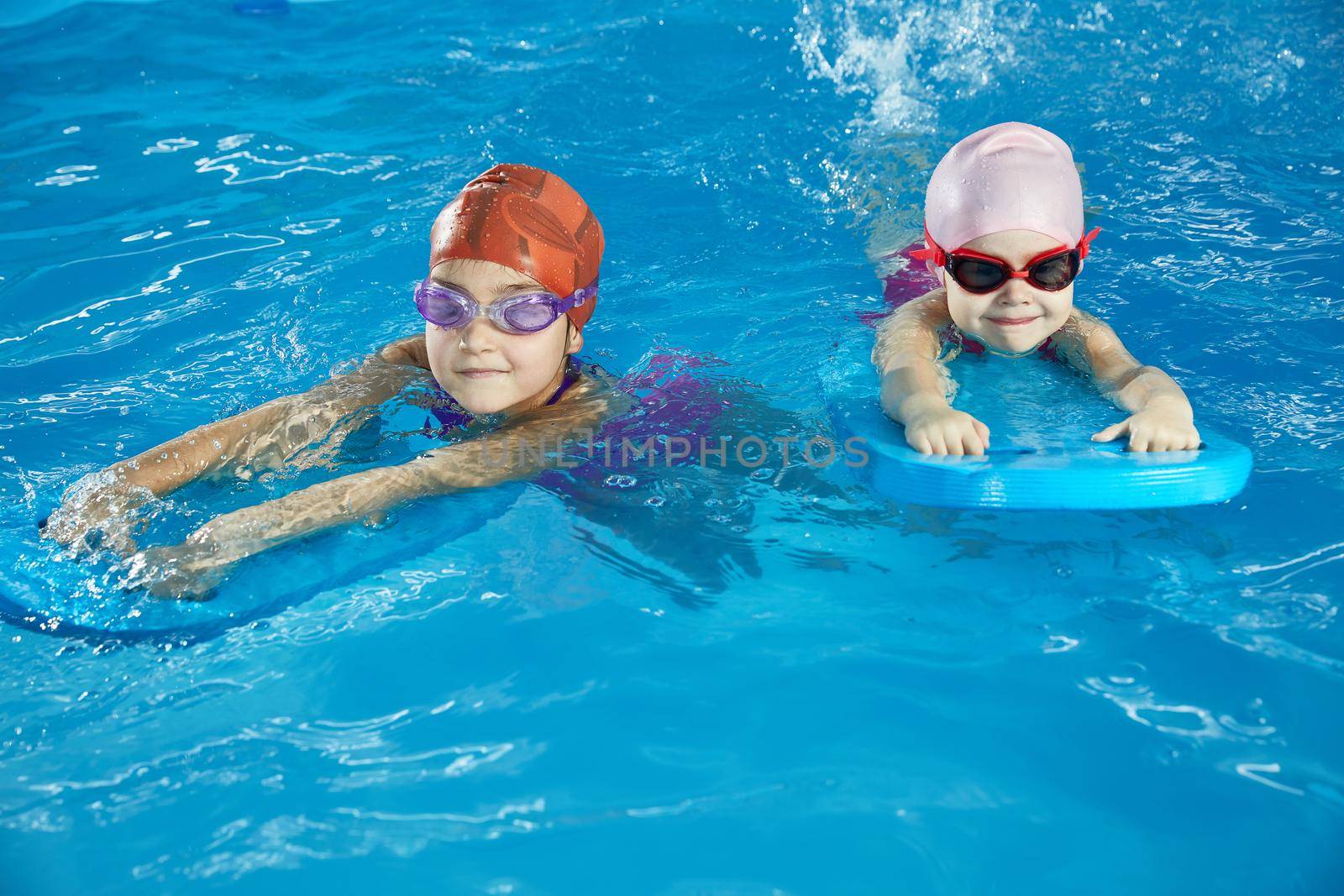 Two little girls learning to swim in indoor pool with pool board by Mariakray