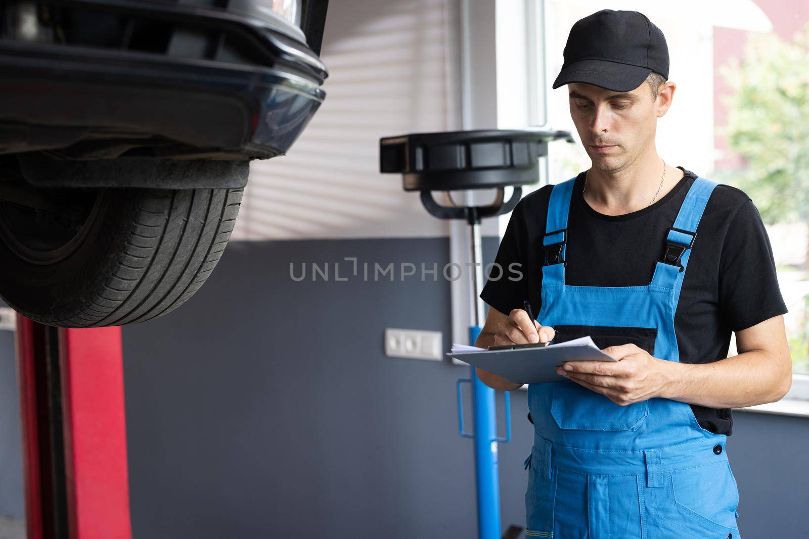 Car mechanic at a repair shop taking notes on his tablet. Automobile service, car mechanic. Car service employe inspect car. Modern clean workshop by uflypro