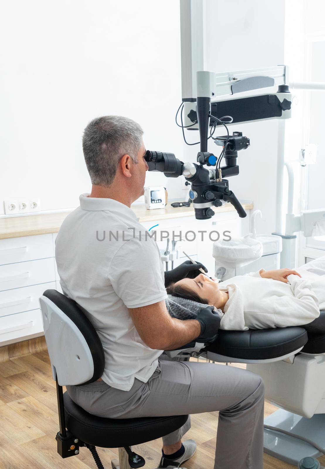 Male dentist using dental microscope treating patient teeth at dental clinic office. Medicine, dentistry and health care concept