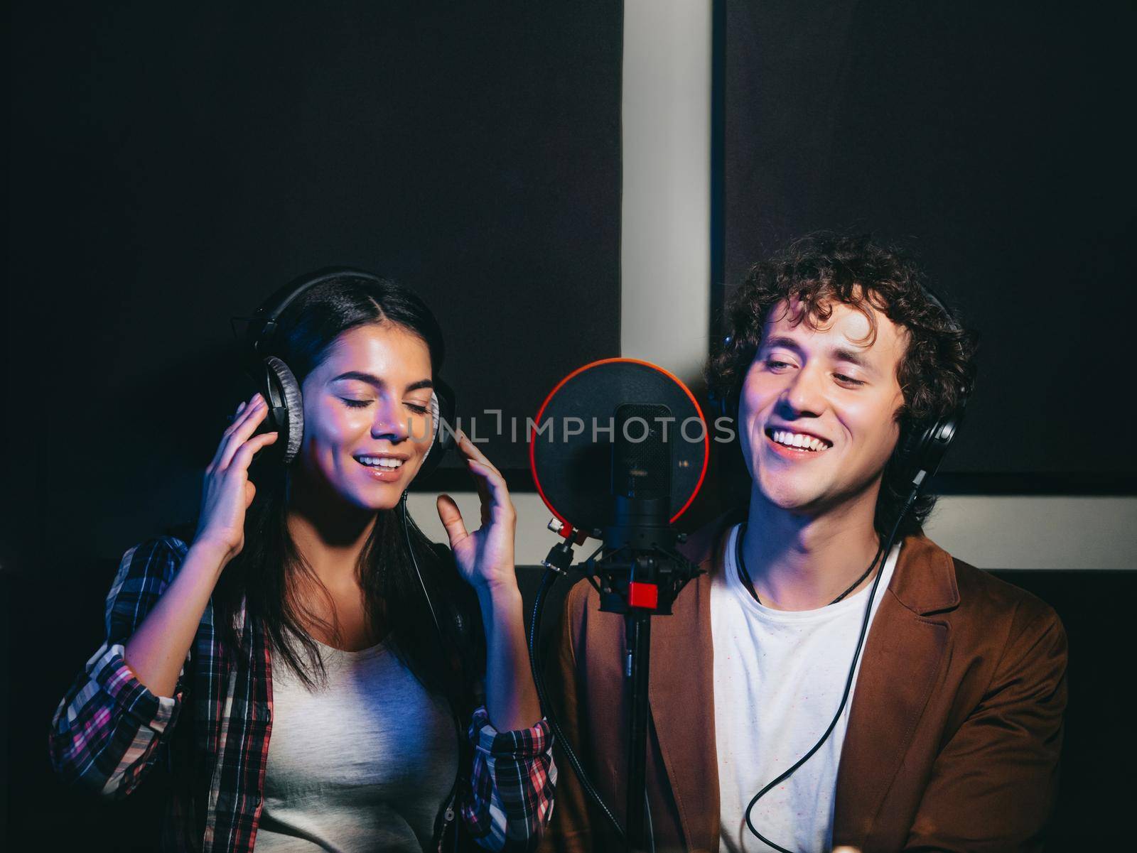 Two young singers performing their song in record studio. Professional musician duet recording new album CD. Beautiful couple working together. High quality photo