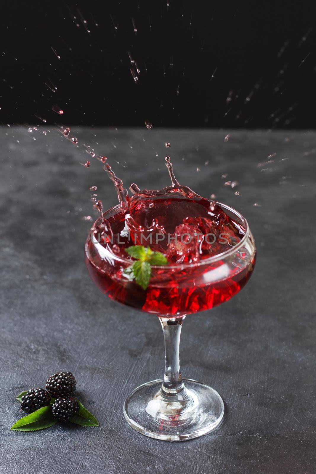 Splash of blackberry cocktail in a glass on a black background.