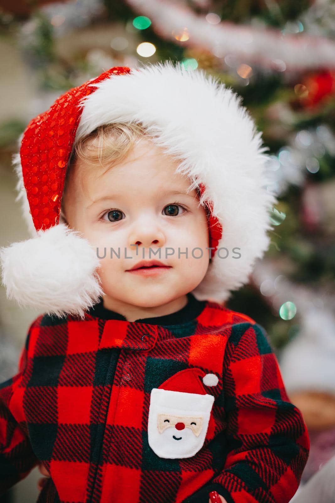 Very cute portrait of little baby boy in Santa hat on Christmas tree lights background bokeh. new year, family, son, toddler child concept