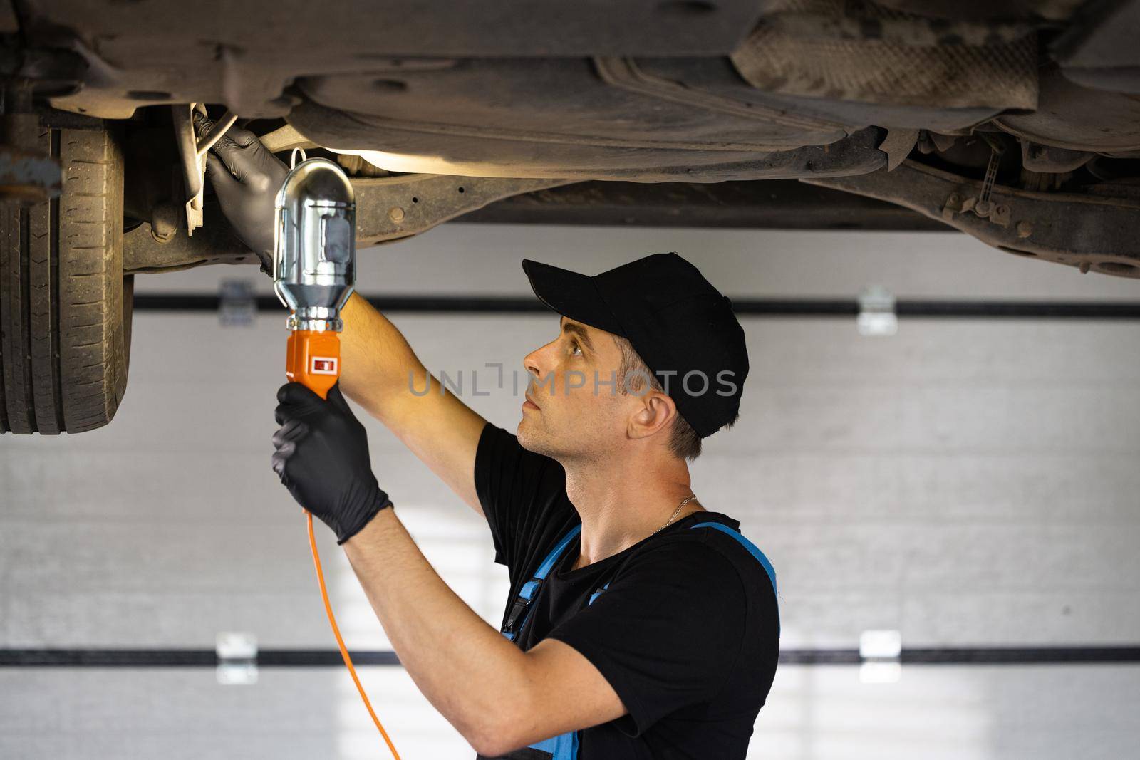 Male car mechanic checking car. Auto mechanic working underneath car lifting machine at the garage. Working in car repair shop and running small feminine business concept.