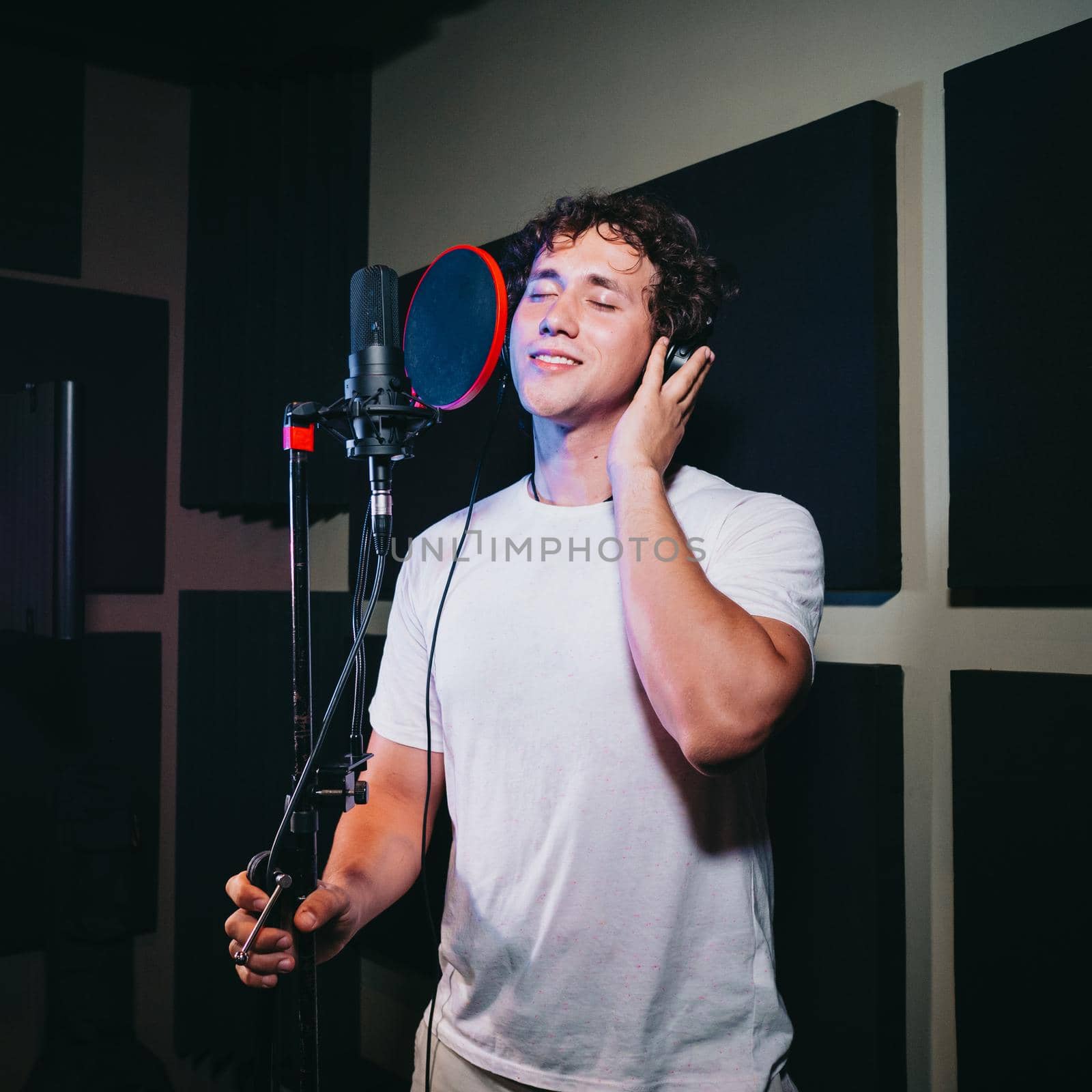 Male vocal artist with curly hair singing alone. Young handsome singer man emotionally writing song in the studio. Recording new melody or album. High quality photo