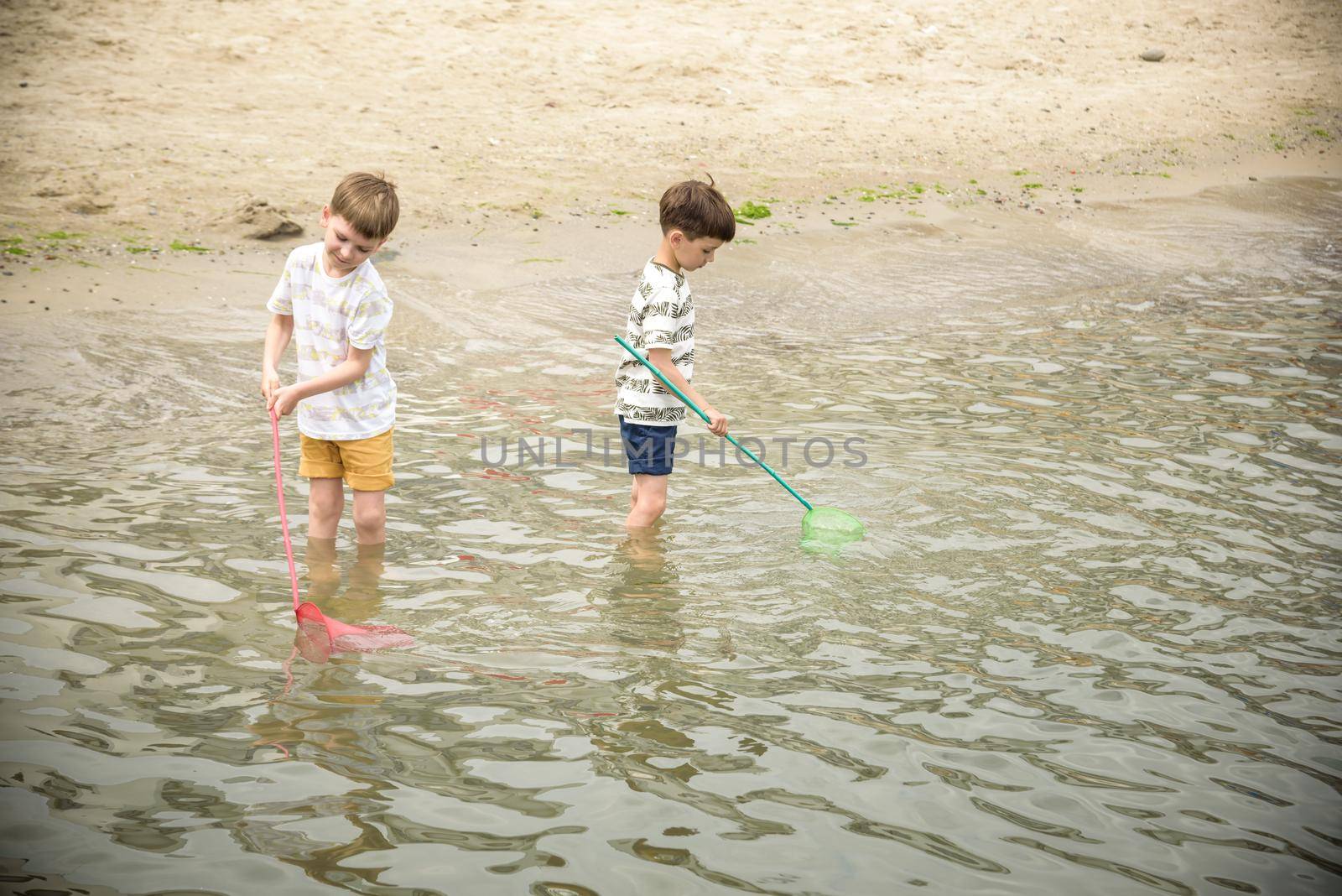 Two sibling little brother boy exploring the beach at low tide walking towards the sea coast. Friendship happy childhood concept.