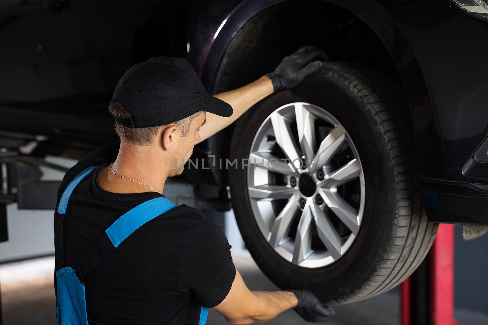 Auto mechanic checking suspension of a lifted car. Experienced car service technician working at the garage. Mechanic repairing car at his workshop. Car on a lift in a specialized service