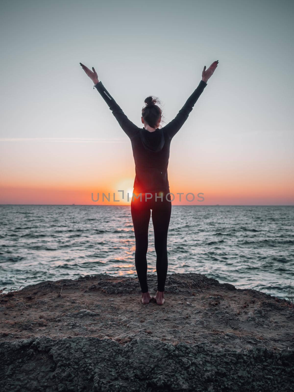 Slim woman in black bodysuit practicing yoga near sea or ocean during sunrise light. Flexibility, stretching, fitness, healthy lifestyle. High quality photo