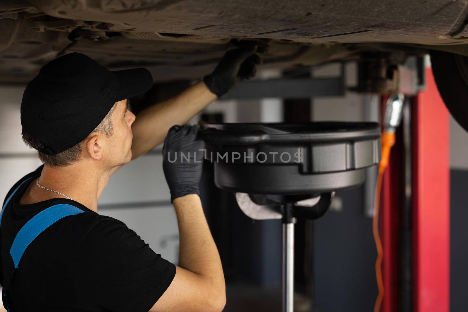 Mechanic drain the old oil from the engine through the drain plug. Changing the oil in a car engine. Car engine oil replacement. Car maintenance, car mechanic replaces the oil in the engine by uflypro