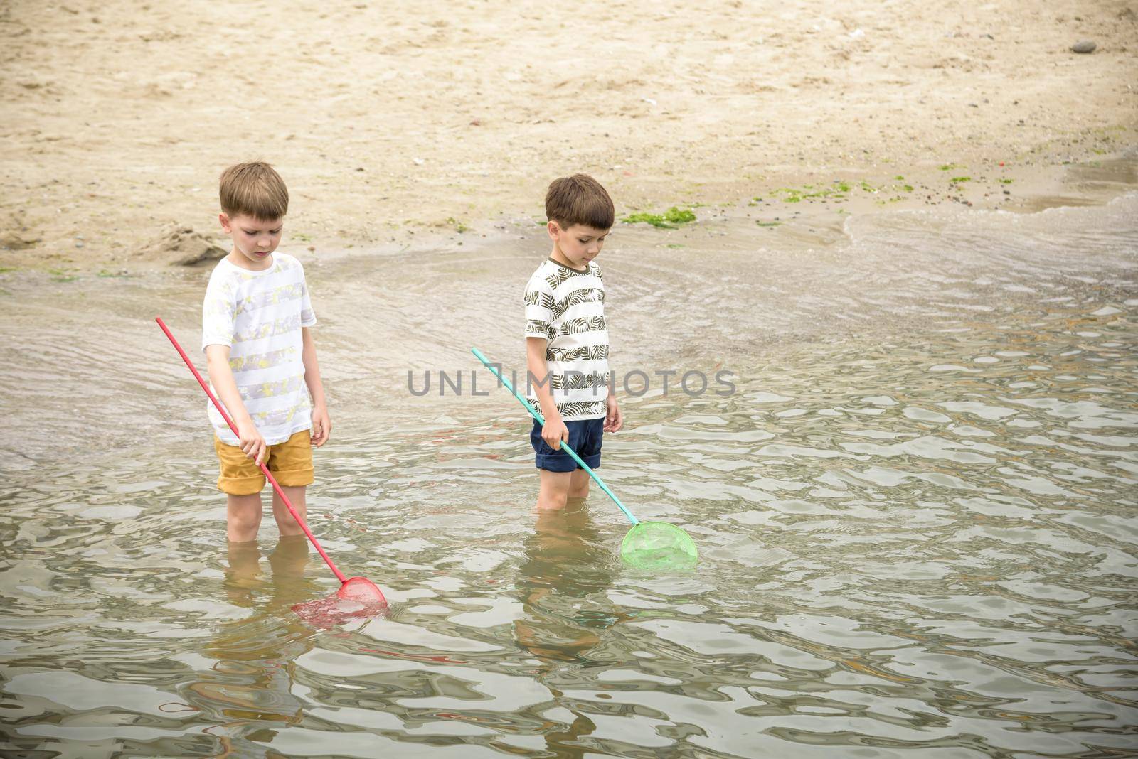 Two sibling little brother boy exploring the beach at low tide walking towards the sea coast. Friendship happy childhood concept by Kobysh