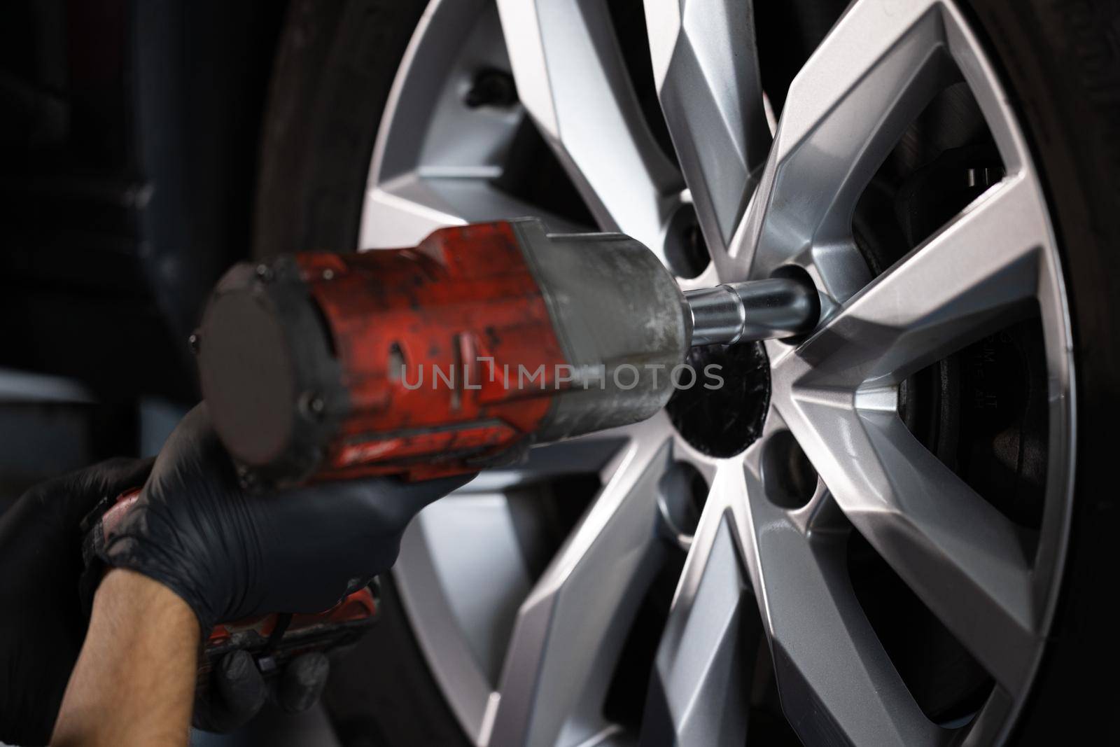 Close up of Mechanic is Unscrewing Lug Nuts with Pneumatic Impact Wrench. Repairman Works in a Modern Car Service. Specialists Removes the Wheel in Order to Fix a Component on a Vehicle by uflypro