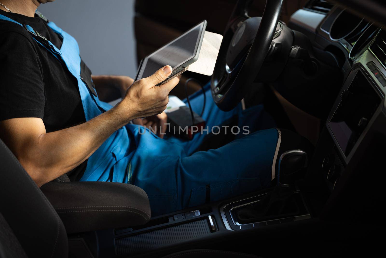 Car mechanic maintains the vehicle with the help of diagnostic modern computer equipment. Car service manager uses tablet computer with diagnostics software.