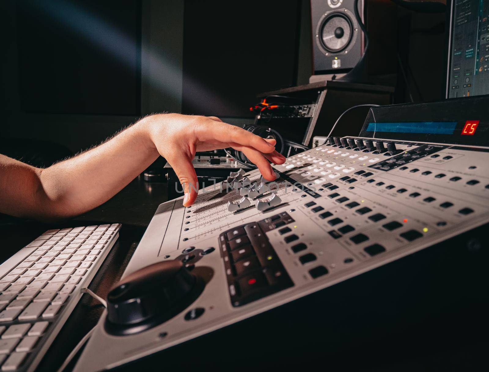 Unrecognizable sound producer or engineer rotates scrolls wheel on mixing console in professional recording studio. Musician working on new song. Hands close up. by kristina_kokhanova